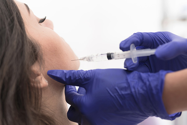 The image shows a person receiving a COVID-19 vaccination from a healthcare worker wearing blue gloves and a face mask, with the individual s head tilted back and a syringe inserted into their arm.