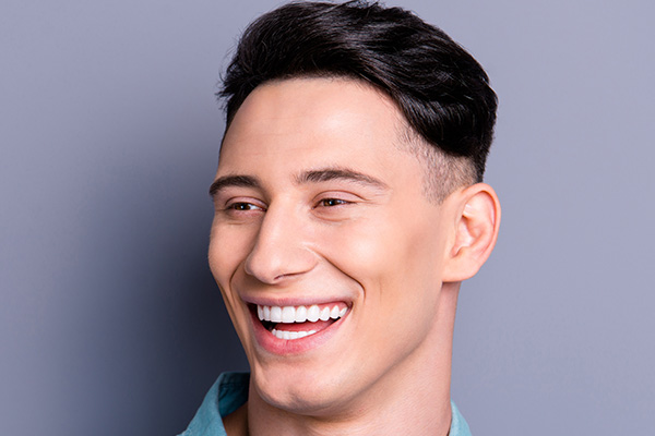 The image shows a young man with short hair and a beard, smiling at the camera, against a neutral background.