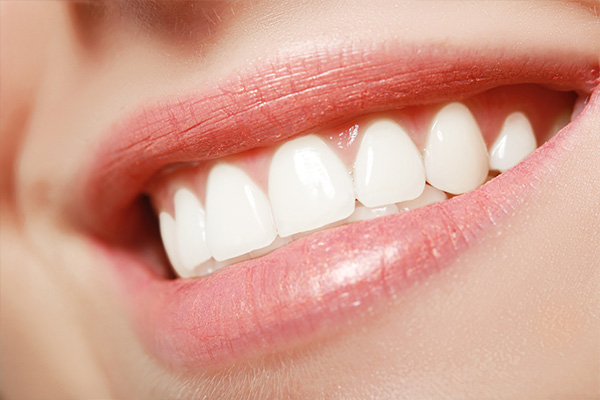 The image shows a close-up view of a smiling person with a pink lipstick, displaying straight white teeth.
