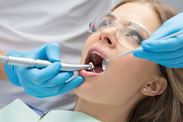 A dental professional using specialized equipment to perform oral care on a patient lying down with their mouth open.