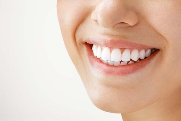 The image shows a close-up of a smiling person with straight teeth, displaying a radiant smile against a white background.