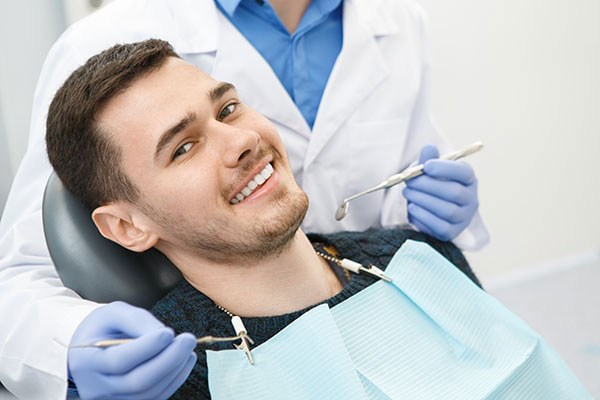 A man sitting in a dental chair with a wide smile, receiving dental care from a professional who is adjusting his mouthpiece.