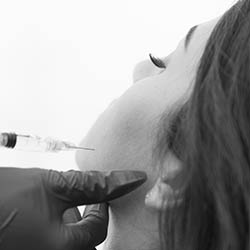 An individual receiving a cosmetic treatment with a needle being injected into their face by a professional.