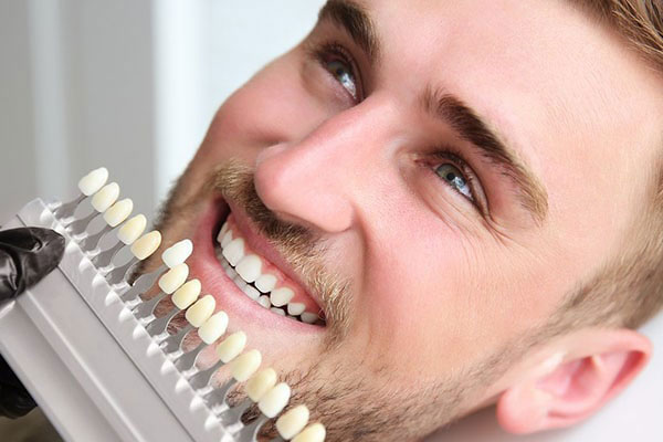 The image features a man with a broad smile, showcasing a set of white teeth, holding a device that appears to be related to dental care or oral health maintenance.