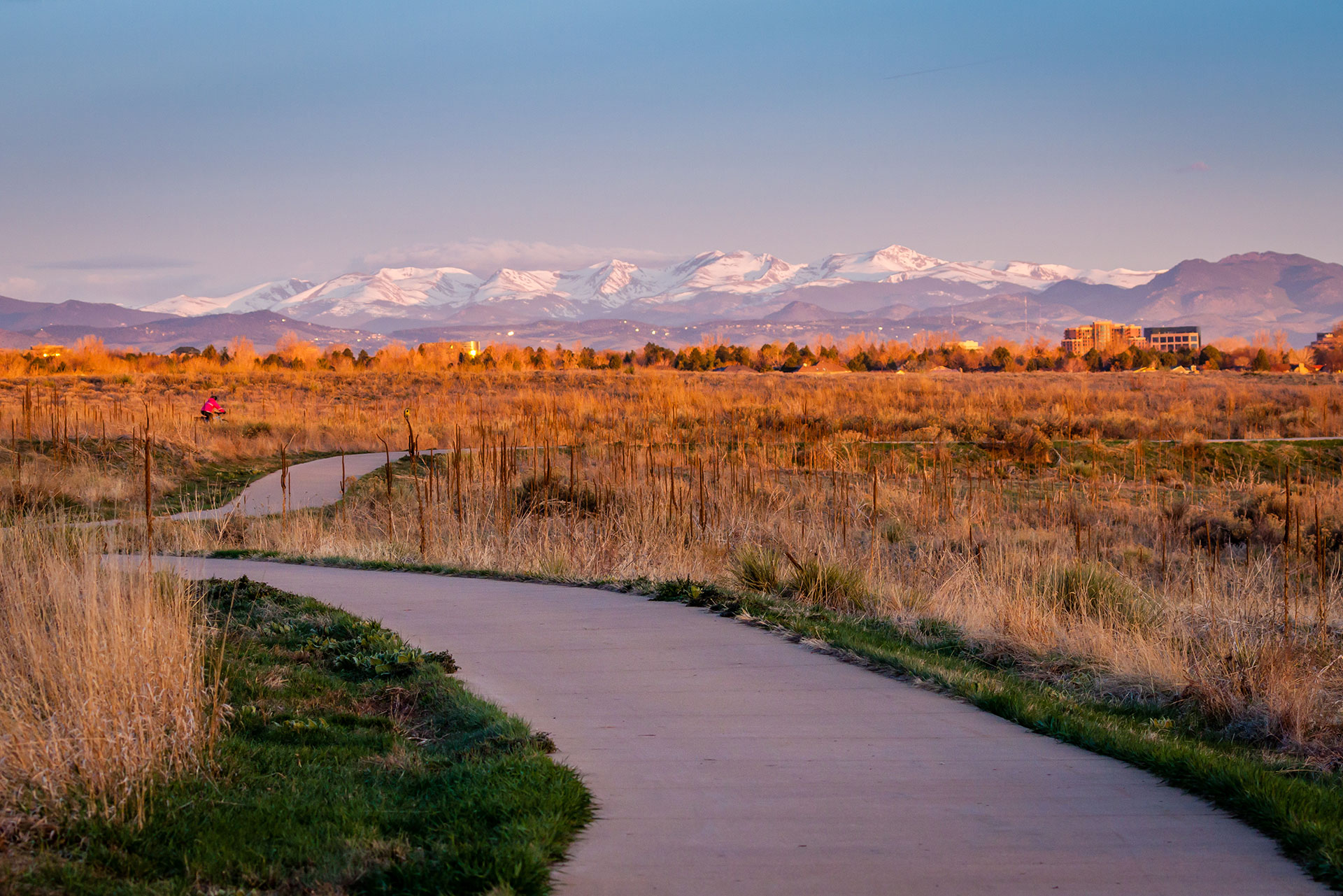 The image shows a path leading towards a scenic landscape with mountains under a clear sky at sunset.