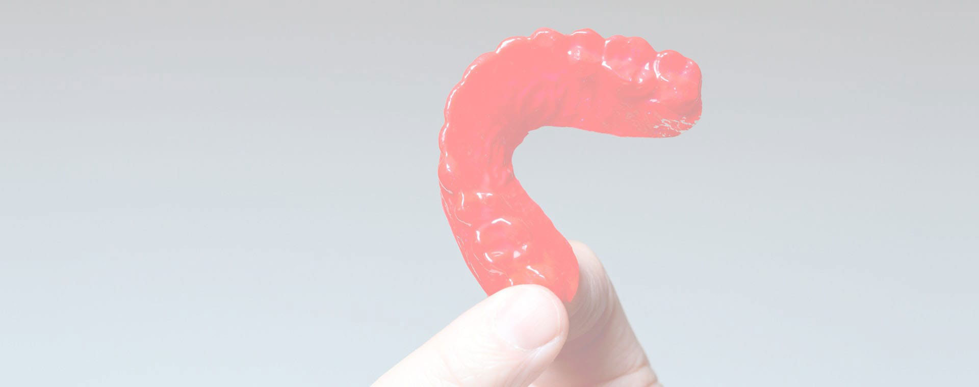 The image shows a red candy cane with a human hand holding it against a plain background.