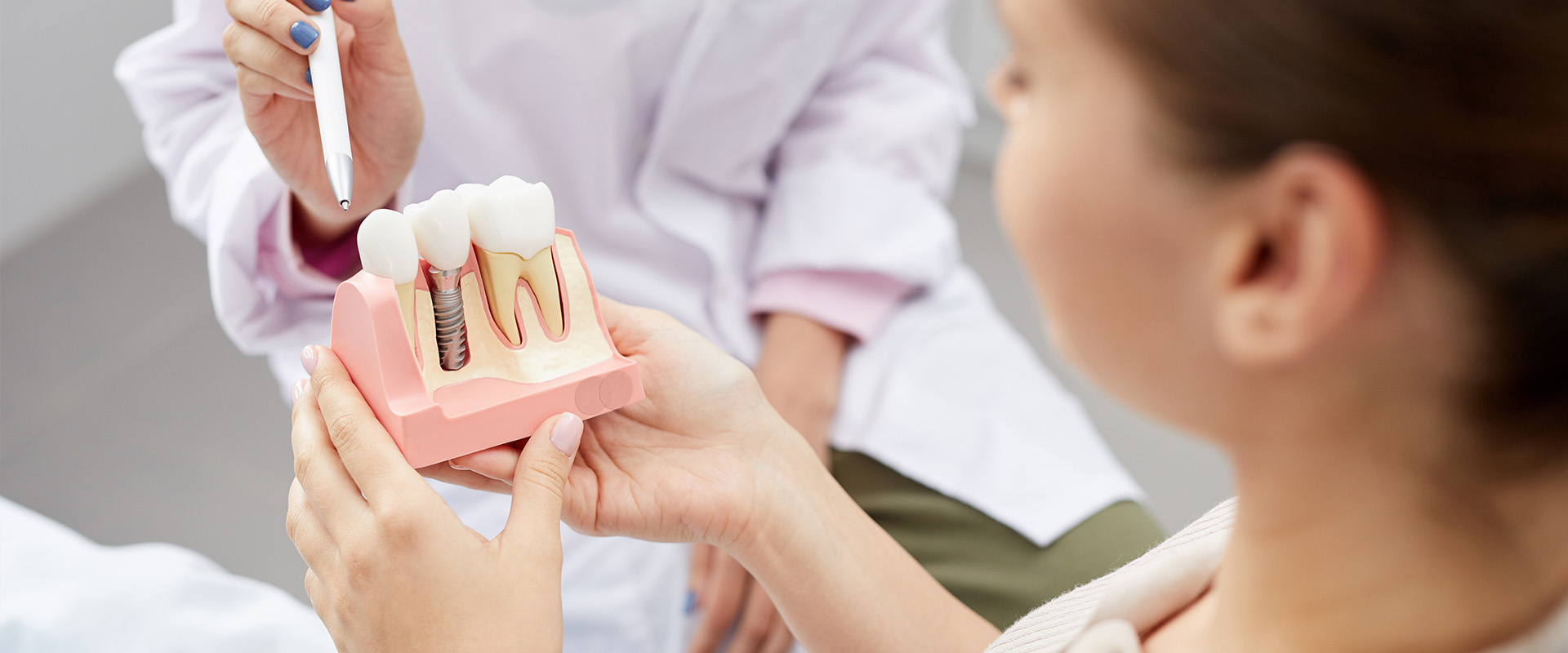 Woman holding pink toothbrush in front of child with open mouth, both standing near dental equipment.
