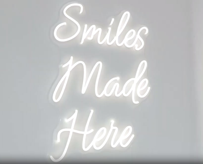 The image features a neon sign with the words  Smiles Made Here  written on it, which is placed against a white background.