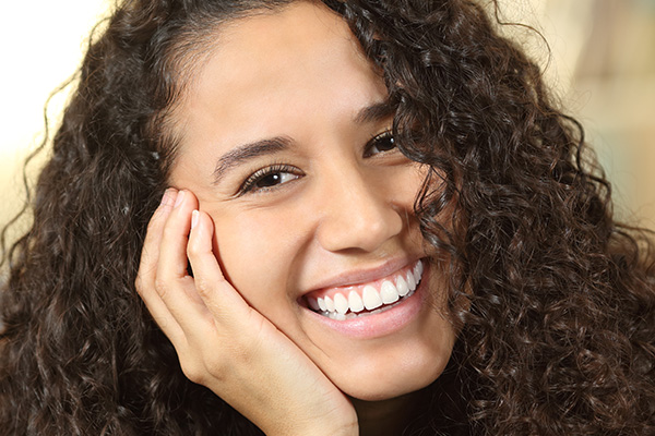 The image shows a smiling woman with curly hair resting her chin on her hand.