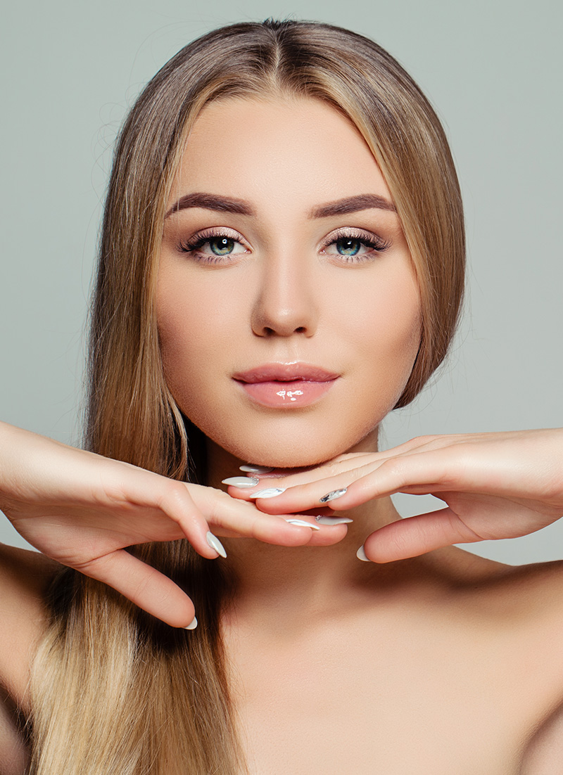 A woman with long hair poses with her hand on her chin, looking directly at the camera.