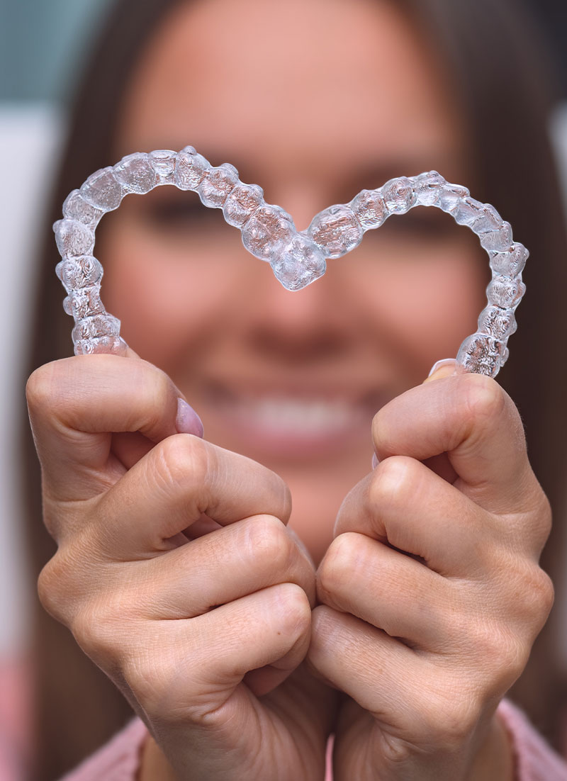 The image shows a person holding up a transparent heart-shaped object with their hands, smiling at the camera.